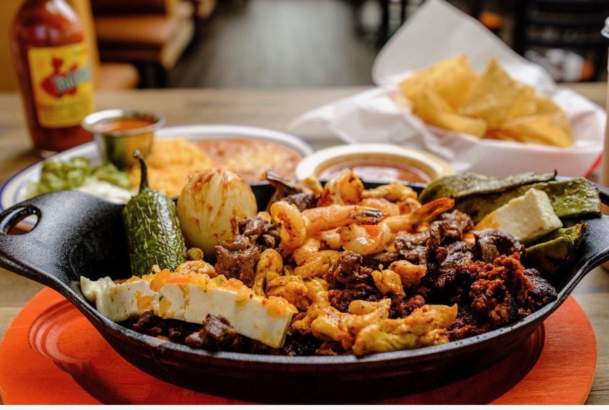 Sizzling molcajete plate with steak, shrimp, chorizo, and queso at Los Primos